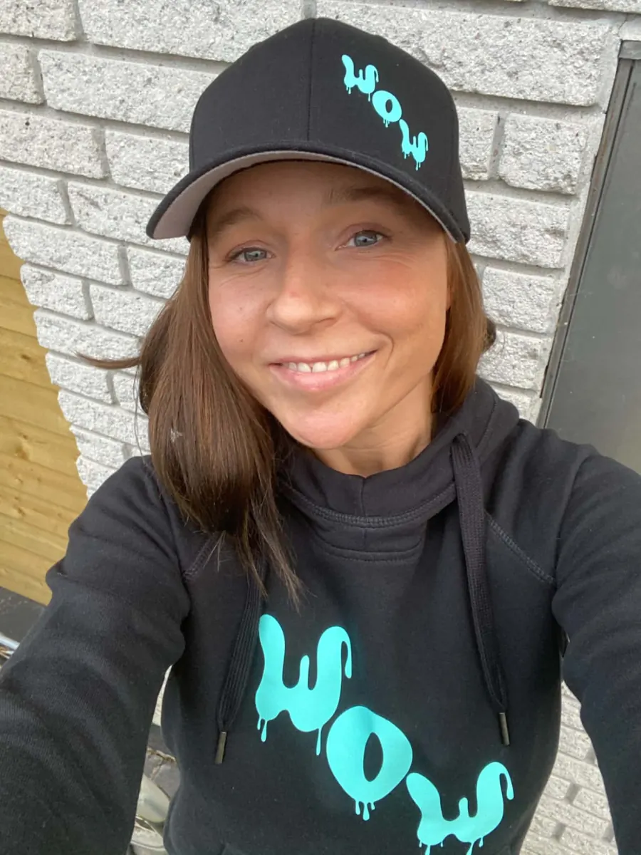 Wicki, ejer og træner hos WOW FIT, i sort WOW-hætte og kasket foran en murstensvæg