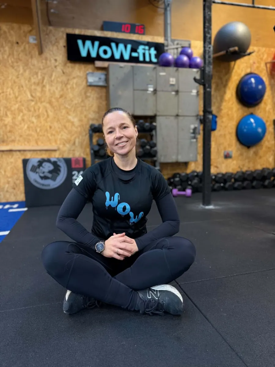 Wicki, ejer og træner hos WOW FIT, sidder på træningsgulvet foran WOW FIT-logoet